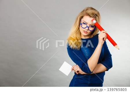 Confused woman holds big pencil note paper in hand Confused woman holds big pencil note paper in hand 139765803