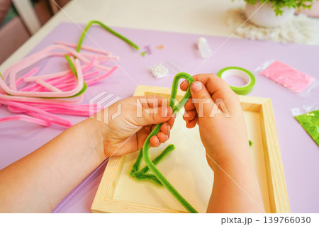 Child shapes fluffy wire into spring flowers. Learning through play boosts dexterity and joy. 139766030
