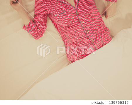 Woman lying on bed wearing pink pajamas Woman lying on bed wearing pink pajamas 139766315