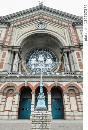 the majestic Victorian architecture of Alexandra Palace, defined by a symmetrical facade of cream stone and terracotta brickwork. In the foreground, an elegant, three-globe blue street lamp stands 139767376
