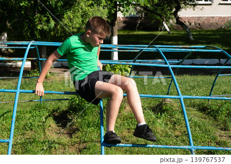 Boy resting on a playground climbing frame outdoors on a sunny day. Boy resting on a playground climbing frame outdoors on a sunny day. 139767537