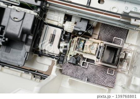 Close-up of a printer printhead and internal mechanism showing ink residue, gears and components, illustrating maintenance, repair, cleaning and diagnostic work on office equipment and electronics. 139768801