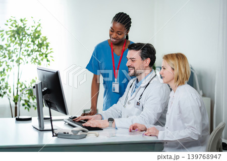 Medical team collaborating on computer in clinic office Medical team collaborating on computer in clinic office 139768947