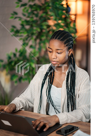 Young black woman telecommuting at home office using laptop Young black woman telecommuting at home office using laptop 139768970