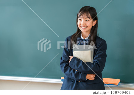 教室の黒板の前で教科書を持つ制服姿の小学生,中学生,高校生の女子生徒 139769402