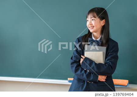 教室の黒板の前で教科書を持つ制服姿の小学生,中学生,高校生の女子生徒 139769404