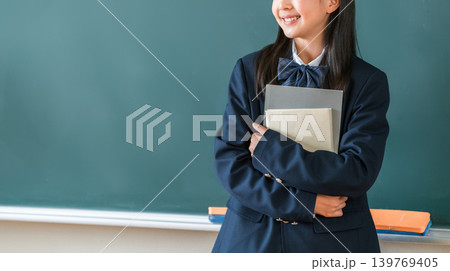 教室の黒板の前で教科書を持つ制服姿の小学生,中学生,高校生の女子生徒 139769405