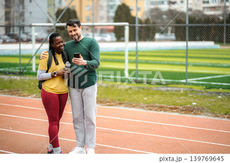 Diverse couple discussing exercise on running track using smartphone Diverse couple discussing exercise on running track using smartphone 139769645