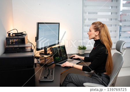 Young adult woman programming on laptop and monitor in modern home office Young adult woman programming on laptop and monitor in modern home office 139769725
