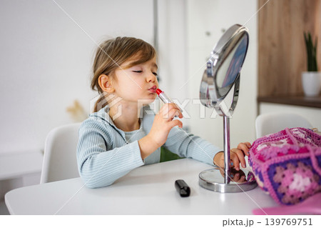 Little girl applying lipstick looking in mirror 139769751