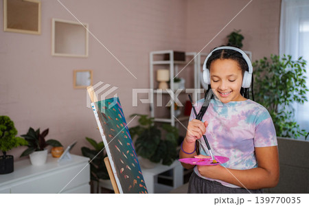 Young girl painting on canvas wearing headphones at home Young girl painting on canvas wearing headphones at home 139770035