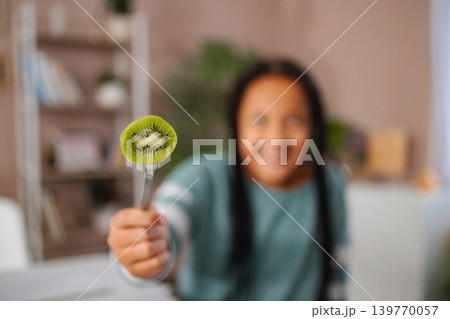 Young girl holding kiwi fruit on fork offering healthy snack Young girl holding kiwi fruit on fork offering healthy snack 139770057
