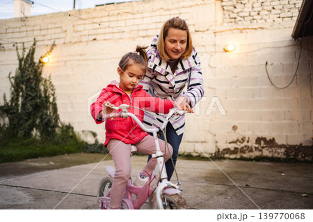 Mother teaching daughter riding bicycle outdoors Mother teaching daughter riding bicycle outdoors 139770068