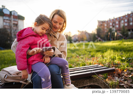 Mother and daughter using phone together in park Mother and daughter using phone together in park 139770085
