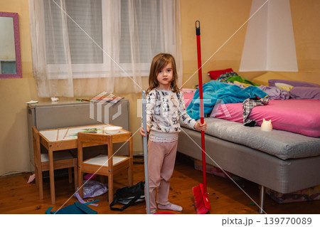 Young girl holding broom and mop cleaning messy bedroom Young girl holding broom and mop cleaning messy bedroom 139770089