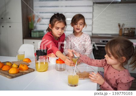Three young girls enjoying making fresh orange juice in kitchen 139770103