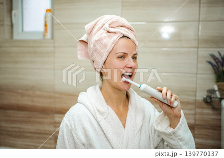 Woman brushing teeth with electric toothbrush during morning routine Woman brushing teeth with electric toothbrush during morning routine 139770137