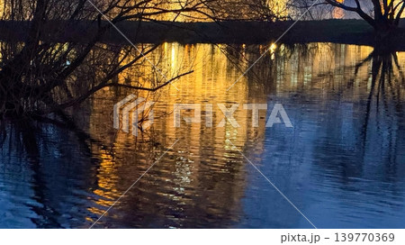 Nature Background with City Lights Reflecting in Pond Water at Night in Urban Park Nature Background with City Lights Reflecting in Pond Water at Night in Urban Park 139770369