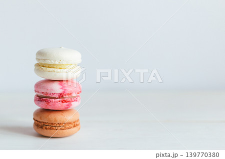 Three French macarons on a white wooden table. Multicolored macarons. Minimal concept. Three French macarons on a white wooden table. Multicolored macarons. Minimal concept. 139770380