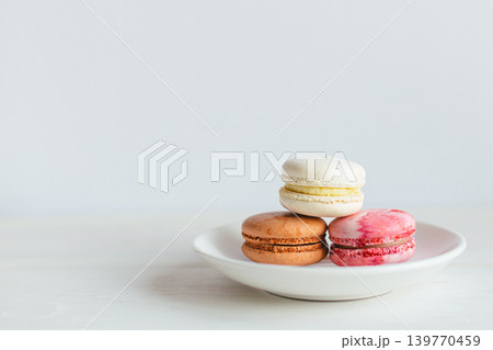 Three French macarons on a white plate. Multicolored macarons. Minimal concept. Three French macarons on a white plate. Multicolored macarons. Minimal concept. 139770459