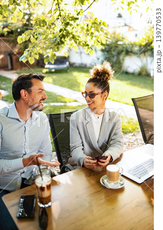 Business colleagues having outdoor coffee meeting discussing work Business colleagues having outdoor coffee meeting discussing work 139770533