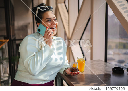 Smiling woman enjoying a drink while chatting on the phone Smiling woman enjoying a drink while chatting on the phone 139770596