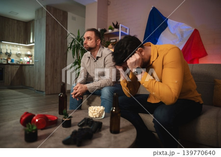 Friends in deep thought during an intense sporting event at home, surrounded by snacks and drinks late at night 139770640