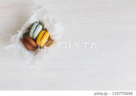 Three French macarons in gift box on a white wooden table. Chocolate, yellow and light blue macarons. 139770898