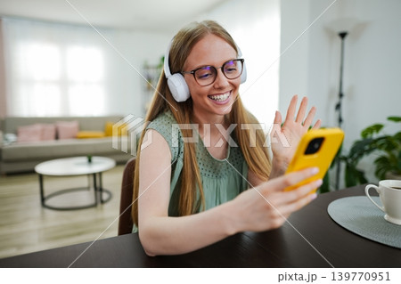 Smiling girl enjoying a video call while wearing headphones indoors 139770951