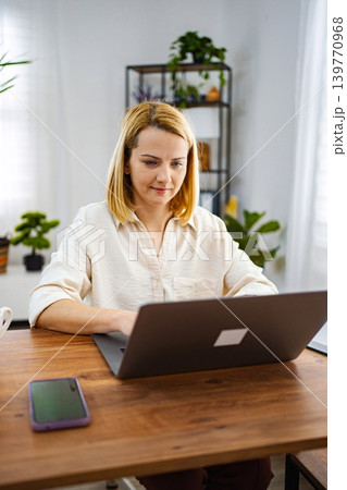 Woman working intently on a laptop in a bright room Woman working intently on a laptop in a bright room 139770968