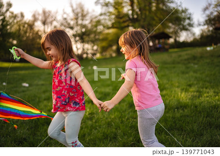 Sisters joyfully running together with a colorful kite in the park Sisters joyfully running together with a colorful kite in the park 139771043