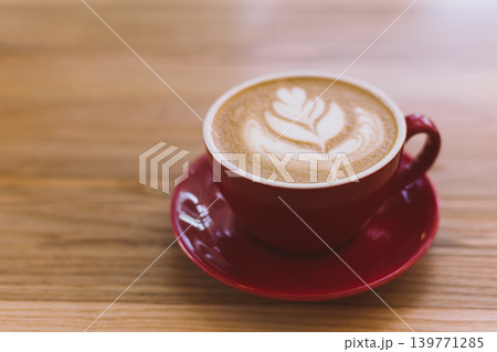 Cup of cappuccino with latte art on wooden background. Red ceramic cup. 139771285