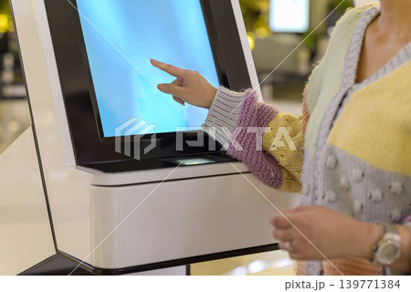 Close-up of a person's hand interacting with a digital touch screen on a modern white self-service kiosk, likely for check-in or service in a public place Close-up of a person's hand interacting with a digital touch screen on a modern white self-service kiosk, likely for check-in or service in a public place 139771384