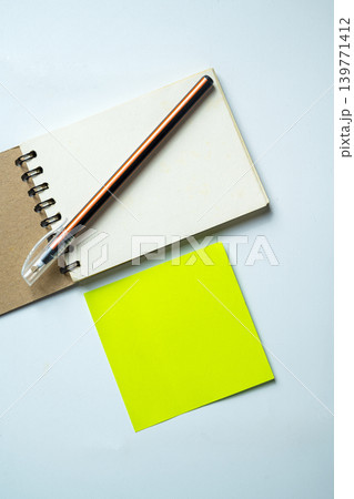 Top-down view of essential office supplies featuring a small spiral notebook, a pen, and a bright neon green adhesive sticky note on a textured gray background Top-down view of essential office supplies featuring a small spiral notebook, a pen, and a bright neon green adhesive sticky note on a textured gray background 139771412