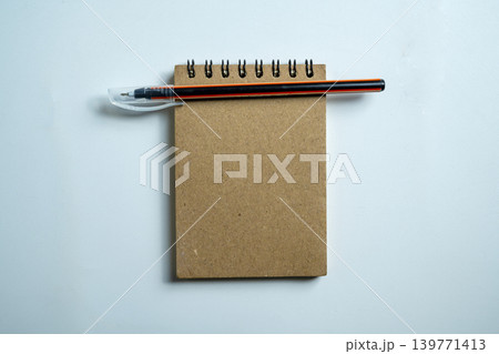 A top-down view of a blank brown spiral-bound notepad with an orange and black pen resting on it, set against a neutral gray textured background A top-down view of a blank brown spiral-bound notepad with an orange and black pen resting on it, set against a neutral gray textured background 139771413