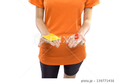 Close up of a referee wearing an orange shirt holding a yellow penalty card and a red whistle in their hands, isolated on white background. Concept of sports competition and fair play 139771438