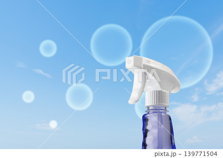 A blue spray bottle with a white trigger nozzle positioned against a bright blue sky with floating soap bubbles, representing fresh and clean household products A blue spray bottle with a white trigger nozzle positioned against a bright blue sky with floating soap bubbles, representing fresh and clean household products 139771504