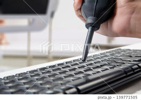 A person uses a manual black rubber air blower pump to remove dust and debris from between the keys of a computer keyboard in an office environment A person uses a manual black rubber air blower pump to remove dust and debris from between the keys of a computer keyboard in an office environment 139771505