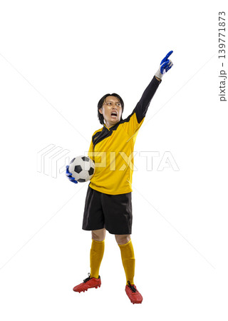 Professional Indonesian southeast asian soccer goalkeeper in a yellow uniform holding a ball and pointing upwards while shouting with passion, isolated on a white background 139771873