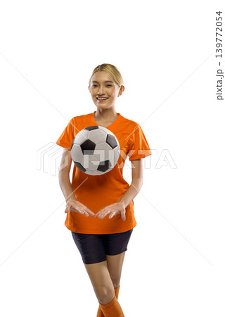 A cheerful Indonesian southeast asian woman in an orange sports uniform juggling a soccer ball against a white background, demonstrating fitness, athletic skill, and a healthy active lifestyle A cheerful Indonesian southeast asian woman in an orange sports uniform juggling a soccer ball against a white background, demonstrating fitness, athletic skill, and a healthy active lifestyle 139772054