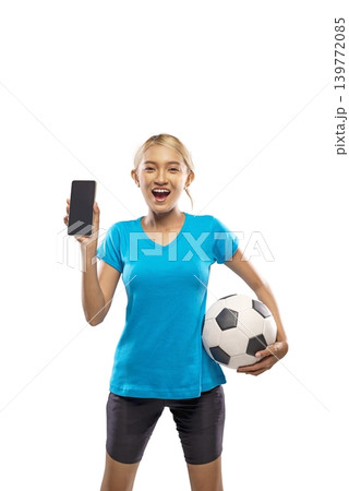 Enthusiastic young Indonesian southeast asian woman holding a soccer ball and showing a smartphone screen. Studio shot on white background, ideal for sports apps, online betting, and mobile gaming Enthusiastic young Indonesian southeast asian woman holding a soccer ball and showing a smartphone screen. Studio shot on white background, ideal for sports apps, online betting, and mobile gaming 139772085