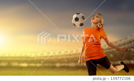 Young Indonesian southeast asian female soccer player in an orange jersey practicing ball control in a large stadium during a vibrant sunset, capturing athletic skill and focus Young Indonesian southeast asian female soccer player in an orange jersey practicing ball control in a large stadium during a vibrant sunset, capturing athletic skill and focus 139772106