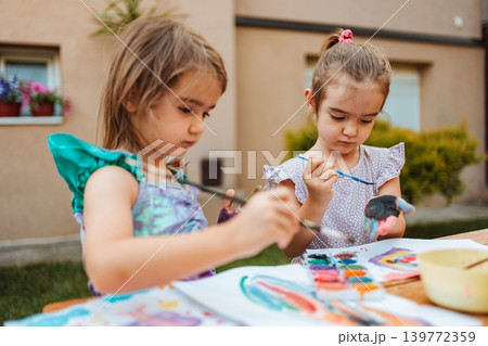 Two preschool girls painting with watercolors in the backyard Two preschool girls painting with watercolors in the backyard 139772359