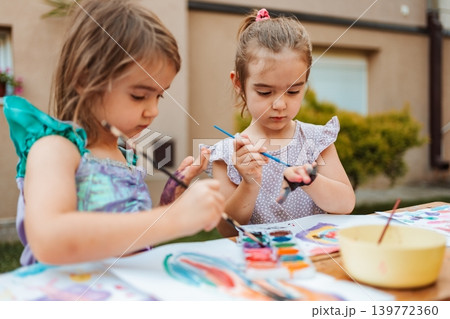 Two preschool girls painting with watercolors in the backyard Two preschool girls painting with watercolors in the backyard 139772360