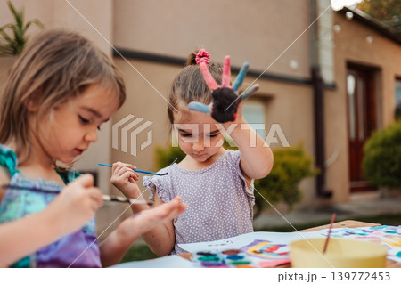 Two little girls enjoying painting outdoors, showing their colorful hands Two little girls enjoying painting outdoors, showing their colorful hands 139772453
