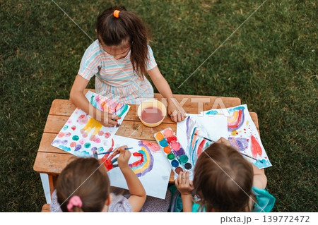Three little girls are painting with watercolors in the garden Three little girls are painting with watercolors in the garden 139772472