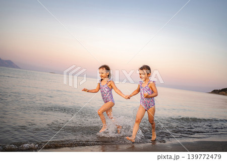 Happy twin sisters holding hands splashing in Greek sea Happy twin sisters holding hands splashing in Greek sea 139772479