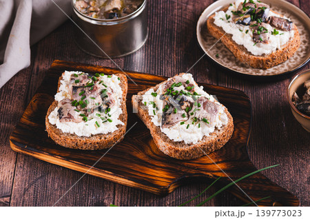 Slices of black bread with ricotta and sardines canned in oil on a board on a table Slices of black bread with ricotta and sardines canned in oil on a board on a table 139773023