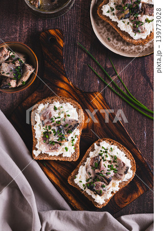 Slices of black bread with ricotta and sardines canned in oil on a board on a table top and vertical view 139773028