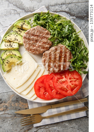 Diet beef burger with cheese, avocado, grilled patty, tomatoes and arugula close-up on a plate. Vertical top view Diet beef burger with cheese, avocado, grilled patty, tomatoes and arugula close-up on a plate. Vertical top view 139773114